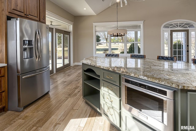 kitchen with appliances with stainless steel finishes, pendant lighting, a notable chandelier, light stone counters, and light hardwood / wood-style flooring