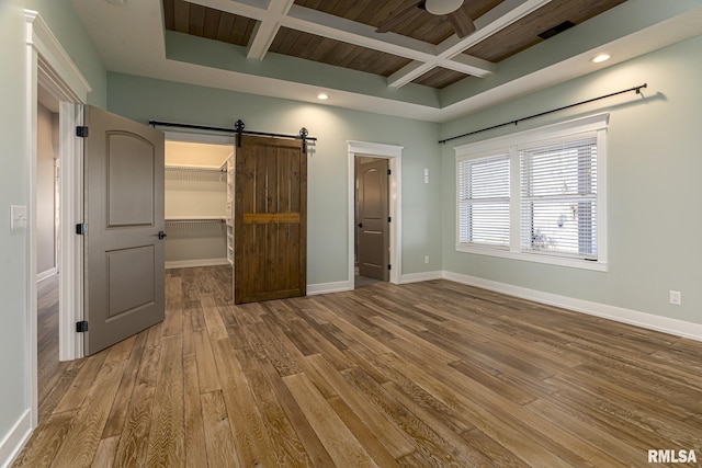 unfurnished bedroom featuring hardwood / wood-style floors, beam ceiling, coffered ceiling, a spacious closet, and a barn door