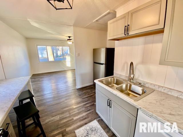 kitchen featuring dishwasher, sink, stainless steel fridge, dark hardwood / wood-style flooring, and light stone countertops