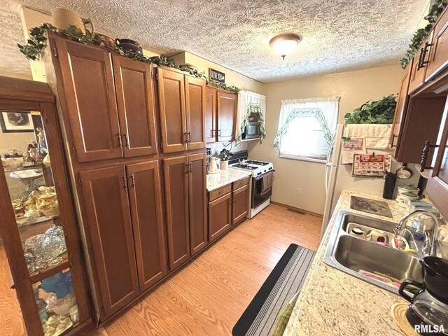 kitchen with sink, white appliances, light stone countertops, a textured ceiling, and light wood-type flooring