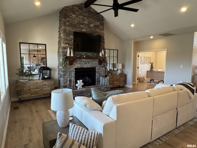 living room featuring ceiling fan, a stone fireplace, light hardwood / wood-style flooring, and beamed ceiling