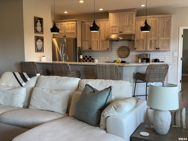 kitchen featuring a kitchen breakfast bar, decorative backsplash, stainless steel refrigerator, and decorative light fixtures