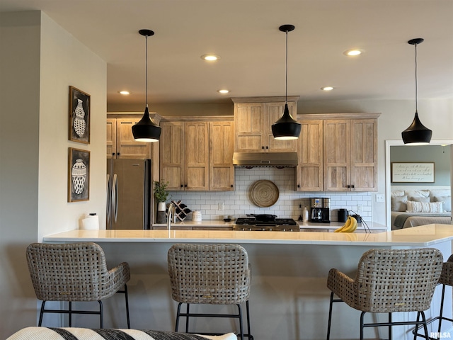 kitchen featuring a kitchen bar, backsplash, stainless steel refrigerator, and decorative light fixtures