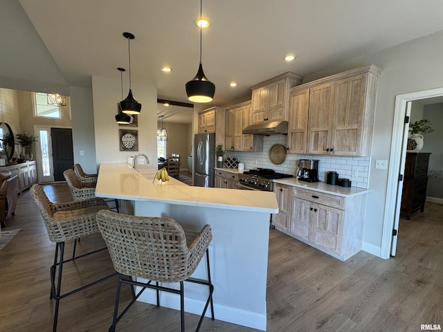 kitchen with a kitchen bar, light brown cabinetry, kitchen peninsula, pendant lighting, and stainless steel appliances