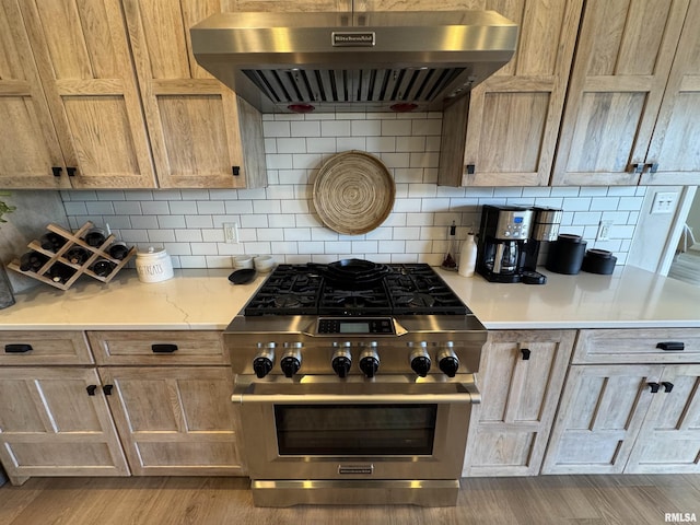 kitchen featuring extractor fan, light stone counters, light wood-type flooring, high end stainless steel range oven, and decorative backsplash