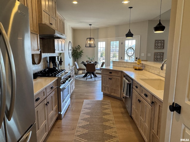 kitchen with sink, tasteful backsplash, decorative light fixtures, light wood-type flooring, and stainless steel appliances