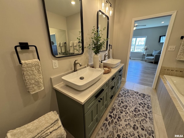 bathroom with a relaxing tiled tub, vanity, and tile patterned flooring