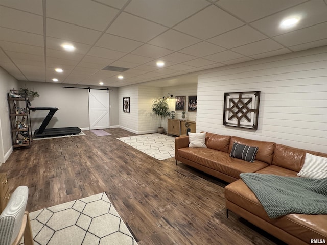 living room with a barn door, dark wood-type flooring, and a paneled ceiling