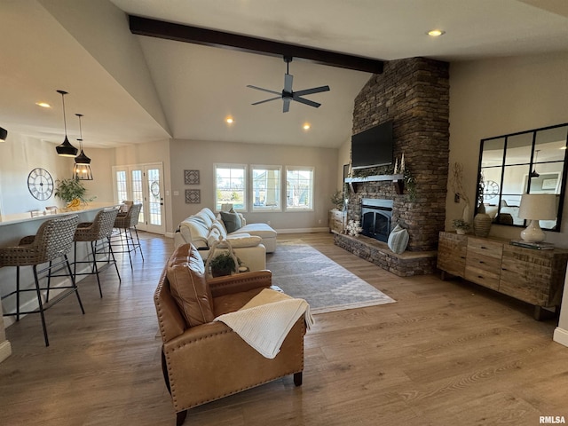 living room with hardwood / wood-style flooring, a stone fireplace, ceiling fan, and beamed ceiling