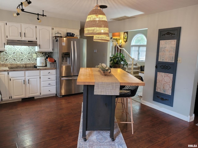 kitchen featuring stainless steel refrigerator with ice dispenser, black electric cooktop, a kitchen breakfast bar, pendant lighting, and white cabinets