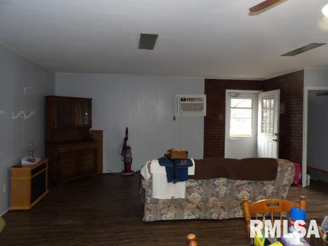 living room featuring dark hardwood / wood-style flooring, a wall unit AC, and ceiling fan