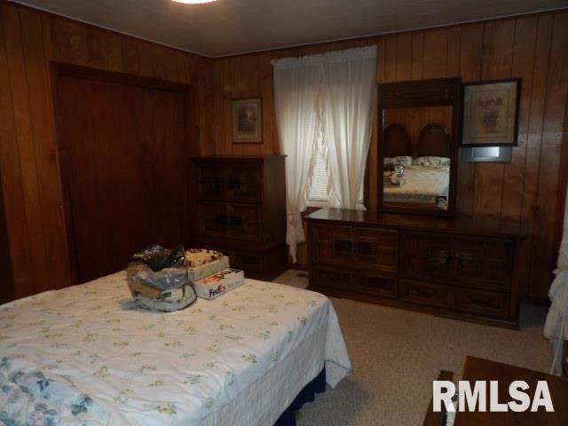 bedroom with wooden walls and light carpet