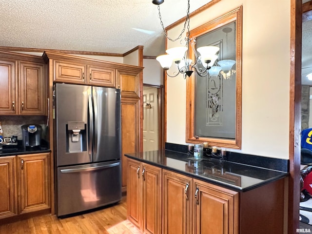 kitchen featuring hanging light fixtures, a textured ceiling, ornamental molding, stainless steel fridge, and light hardwood / wood-style floors