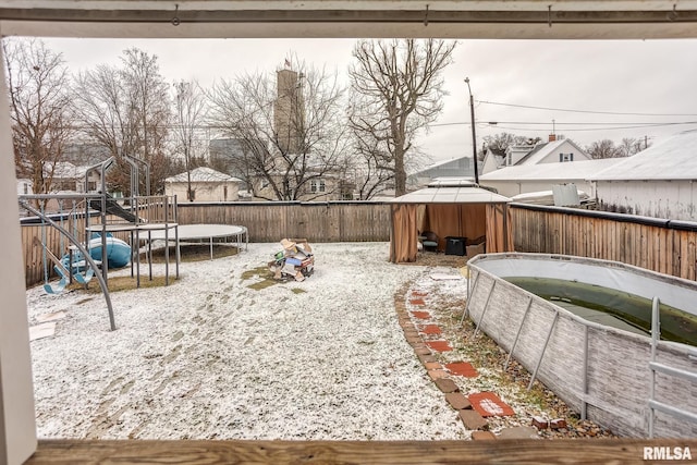 yard layered in snow featuring a gazebo, a playground, and a trampoline