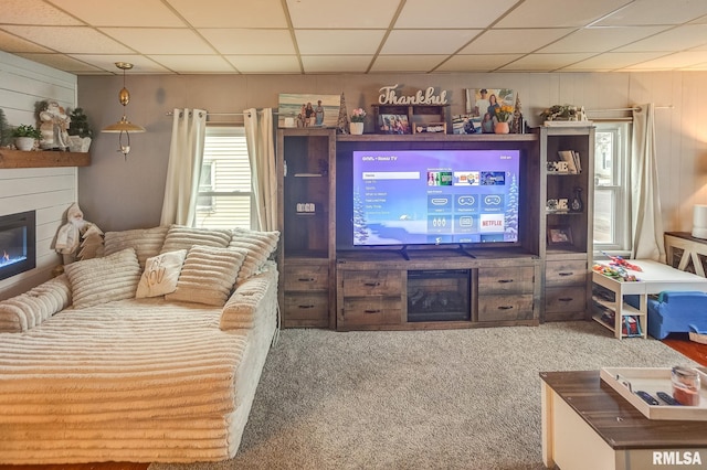 living room with a drop ceiling, carpet floors, and wooden walls