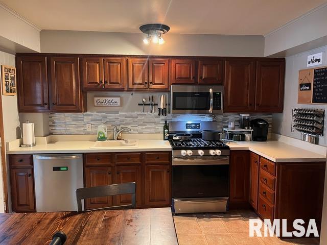 kitchen featuring stainless steel appliances, ornamental molding, sink, and backsplash