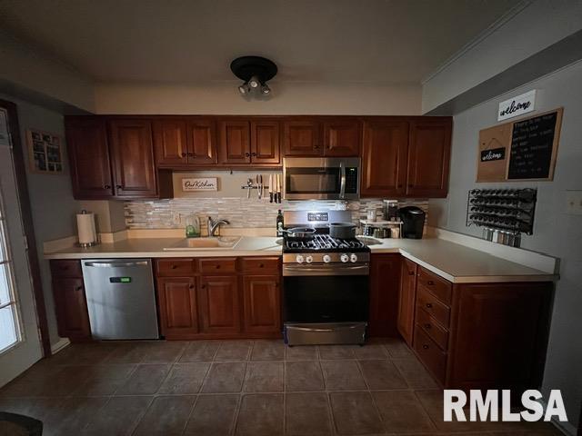 kitchen with sink, backsplash, dark tile patterned floors, and appliances with stainless steel finishes