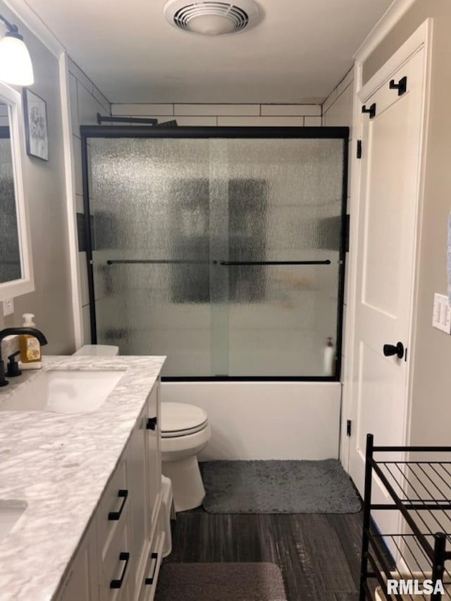 full bathroom featuring vanity, combined bath / shower with glass door, hardwood / wood-style floors, and toilet