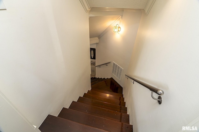 stairway featuring ornamental molding and a textured ceiling