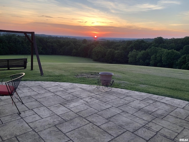 patio terrace at dusk featuring a lawn and a wooded view