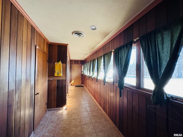 hallway with wood walls, visible vents, and light tile patterned flooring