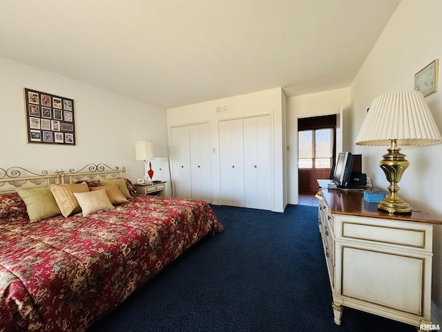 bedroom with multiple closets, dark colored carpet, and visible vents
