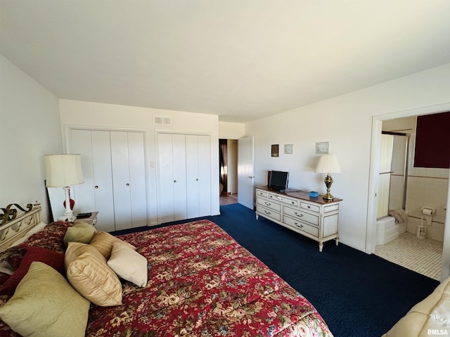 carpeted bedroom featuring visible vents, ensuite bath, and two closets