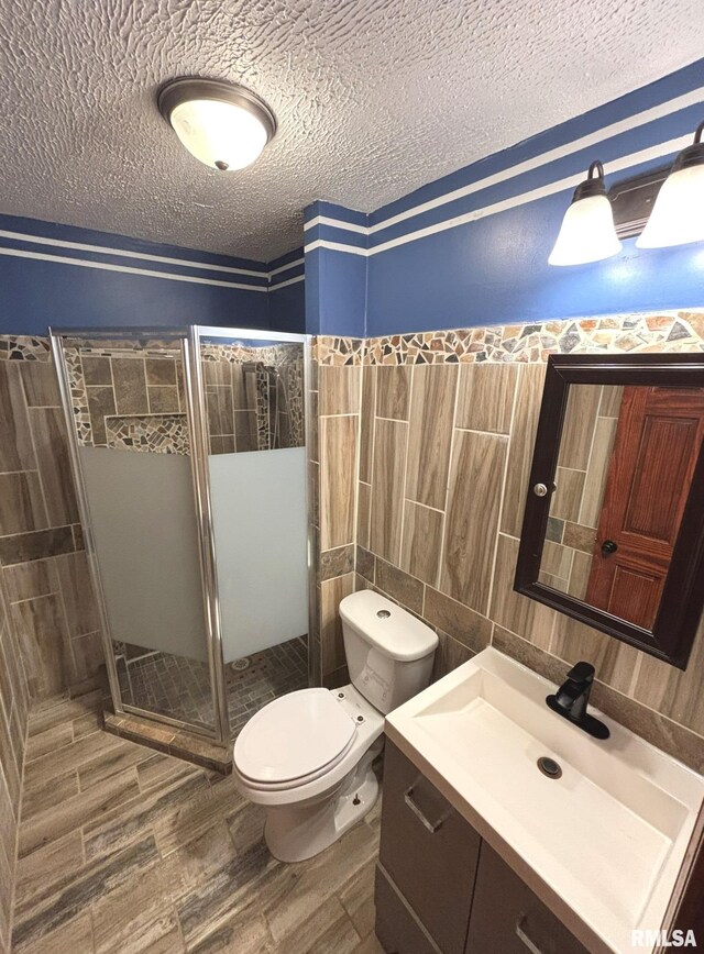 bathroom with toilet, an enclosed shower, tile walls, a textured ceiling, and hardwood / wood-style flooring