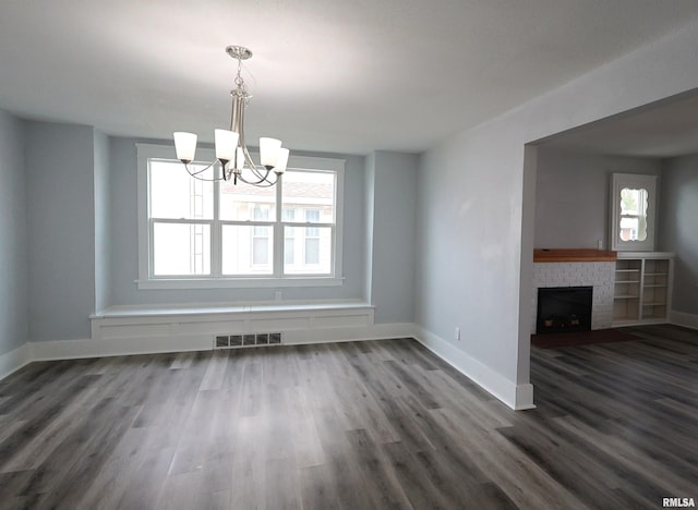 unfurnished dining area featuring dark hardwood / wood-style flooring, a notable chandelier, a fireplace, and a healthy amount of sunlight