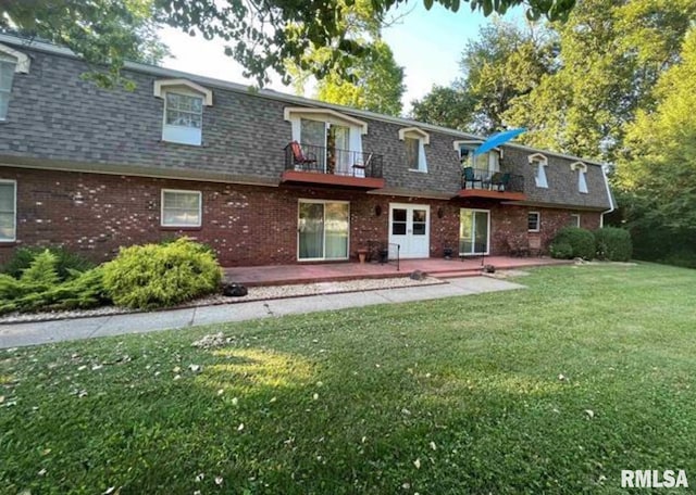 rear view of house with a balcony, a patio, and a lawn