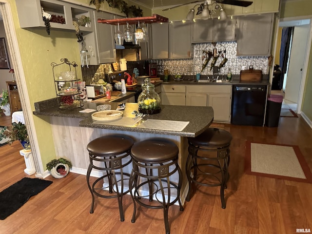 kitchen featuring gray cabinetry, black dishwasher, kitchen peninsula, hardwood / wood-style floors, and backsplash