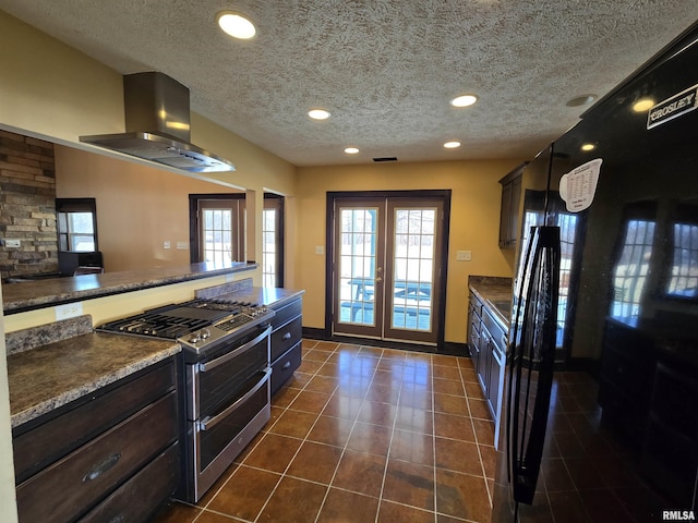 kitchen featuring dark tile patterned floors, double oven range, dark brown cabinetry, ventilation hood, and a textured ceiling