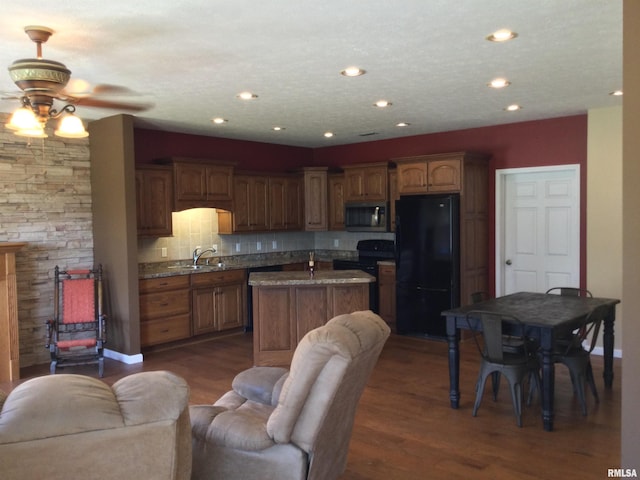 kitchen featuring dark wood-type flooring, backsplash, an island with sink, and black appliances