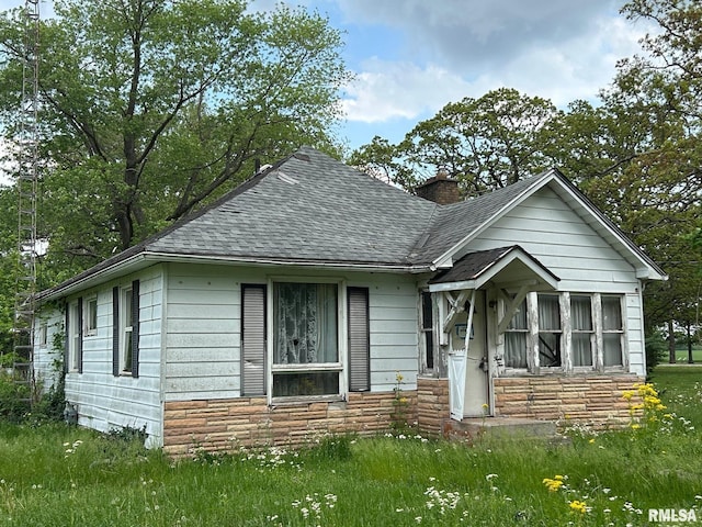 bungalow-style house featuring a shingled roof, a chimney, and stone siding