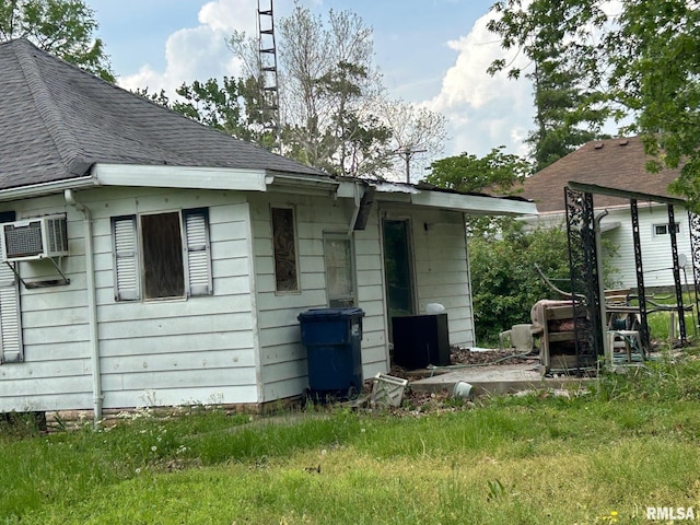 back of house with a wall mounted air conditioner and a shingled roof