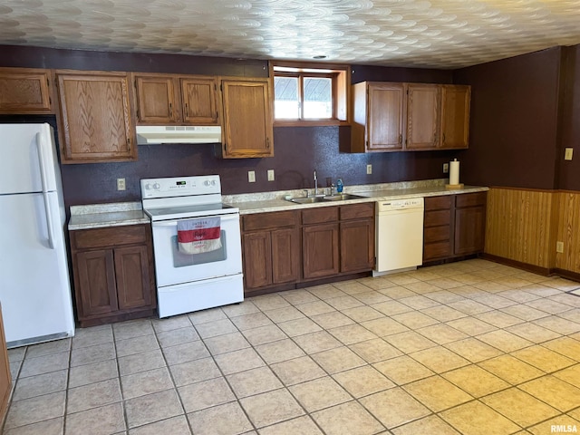 kitchen featuring sink, white appliances, a textured ceiling, and wood walls