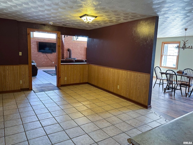 unfurnished room with an inviting chandelier, wooden walls, a textured ceiling, and light tile patterned floors