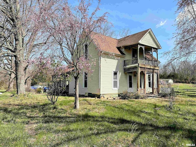 exterior space featuring a balcony, a shingled roof, and a front lawn