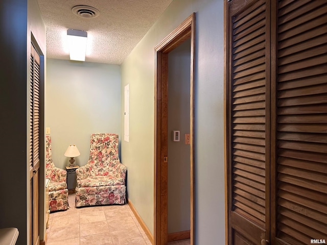 corridor featuring baseboards, visible vents, tile patterned flooring, and a textured ceiling