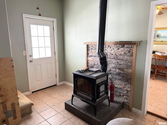 doorway with baseboards, a wood stove, and light tile patterned floors