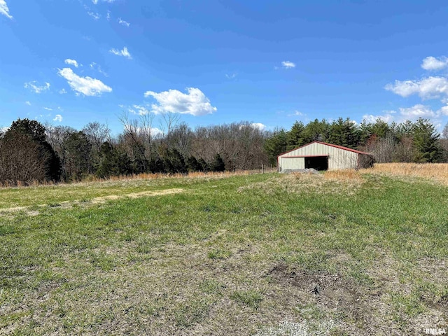 view of yard featuring a detached garage, an outbuilding, a rural view, and a view of trees