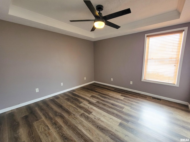 spare room featuring a raised ceiling, ceiling fan, and dark hardwood / wood-style flooring