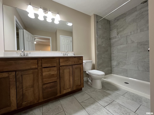 bathroom featuring a sink, a tile shower, toilet, and double vanity