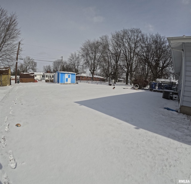 yard layered in snow with a storage unit and central AC