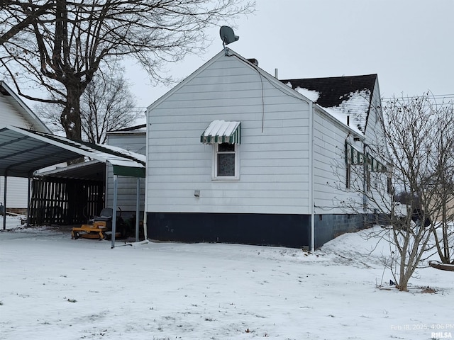 snow covered back of property featuring a carport