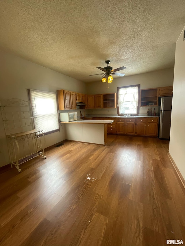 kitchen with brown cabinets, freestanding refrigerator, a peninsula, light countertops, and light wood-type flooring