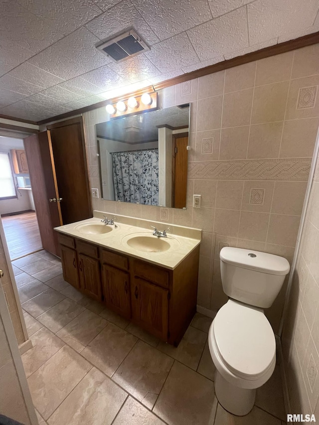 bathroom with toilet, tile walls, visible vents, and a sink