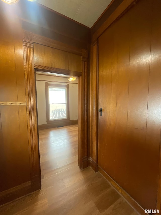 hallway featuring light wood-type flooring and wood walls