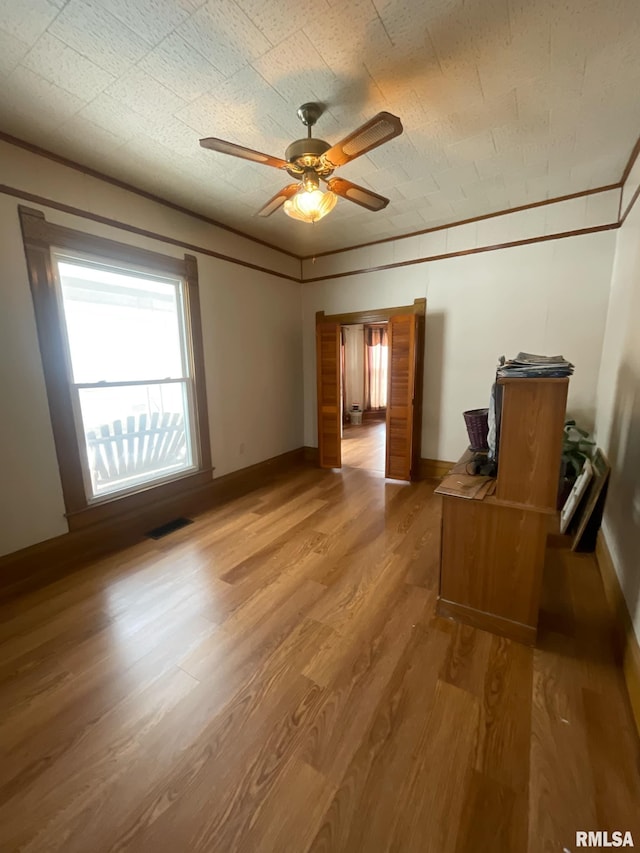 unfurnished bedroom featuring crown molding, visible vents, light wood-style flooring, ceiling fan, and baseboards