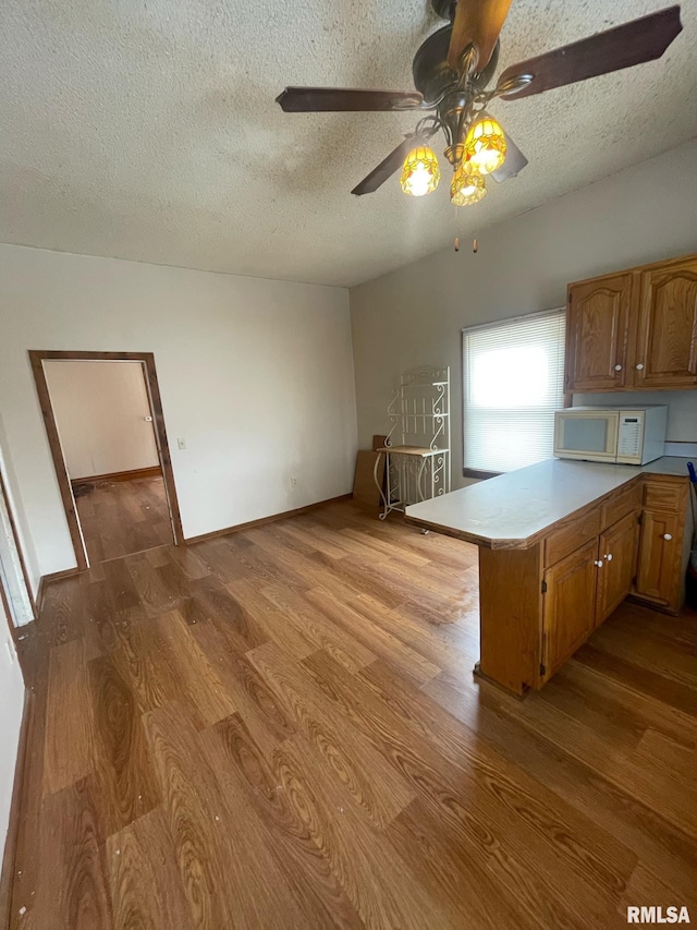 kitchen featuring white microwave, a peninsula, light countertops, light wood finished floors, and brown cabinetry